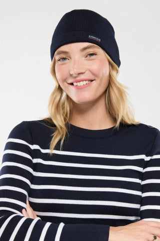 Woman in navy striped sweater and navy knit beanie with small logo, white background