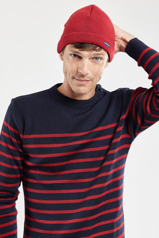 Man wearing a red knit beanie and navy blue sweater with red stripes, posing casually