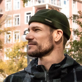 Man wearing a green wool fisherman beanie and plaid jacket outdoors in autumn city