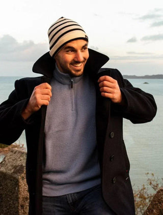 Man outdoors wearing navy wool peacoat, striped beanie, and blue sweater near water