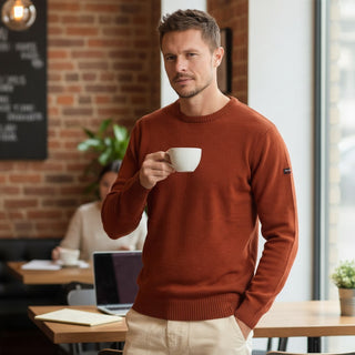 Homme portant un pull Armor-Lux en laine d'agneau couleur ketchup à col rond, style marin, dans un café.