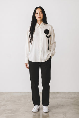 Modèle portant la blouse Le Capitaine D'a Bord blanche à manches longues avec une fleur noire appliquée sur la poitrine