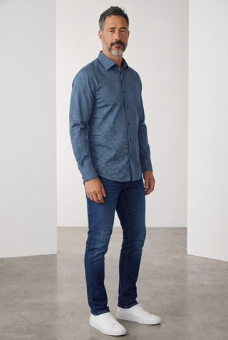 Man wearing a navy blue Bugatchi James long-sleeve shirt with a diamond pattern, paired with jeans and white sneakers.