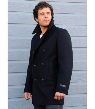 Man wearing navy wool pea coat with double-breasted buttons, standing by gray wall