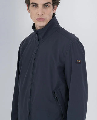 Man wearing dark blue nylon zip-up jacket with high collar and logo patch on sleeve