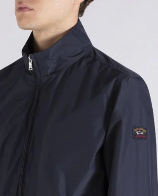 Man wearing a navy nylon zip-up jacket with a logo patch on the sleeve
