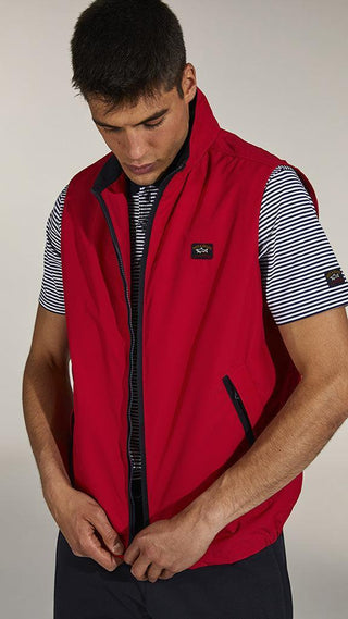 Man wearing a red zip-up nylon vest over a striped short-sleeve shirt
