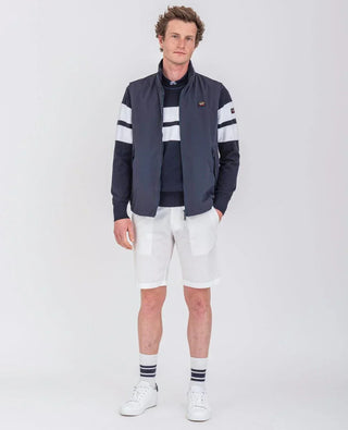 Man wearing navy nylon sleeveless vest, striped navy sweater, white shorts and white sneakers.